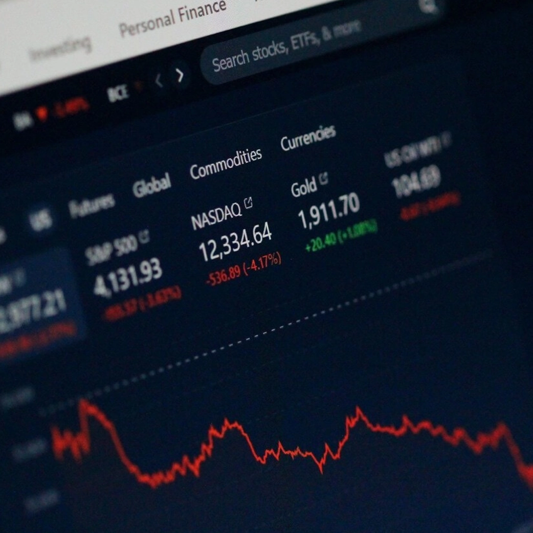 Ecrã com gráfico de ações e cotações de mercado, simbolizando acompanhamento profissional de investimentos.