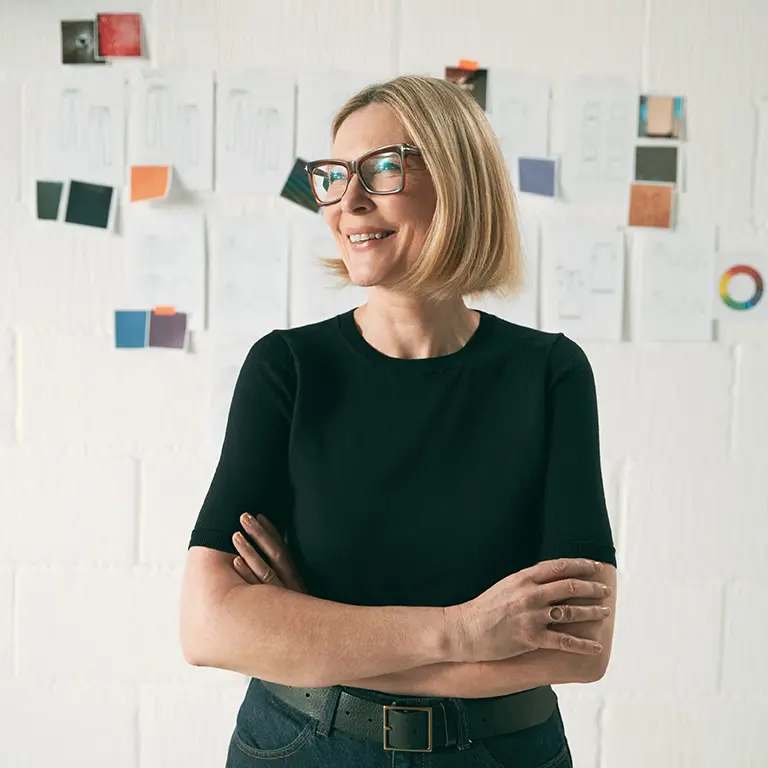 Mulher mais velha à frente de uma parede com alguns post-its, que simbolizam a experiência e conhecimento