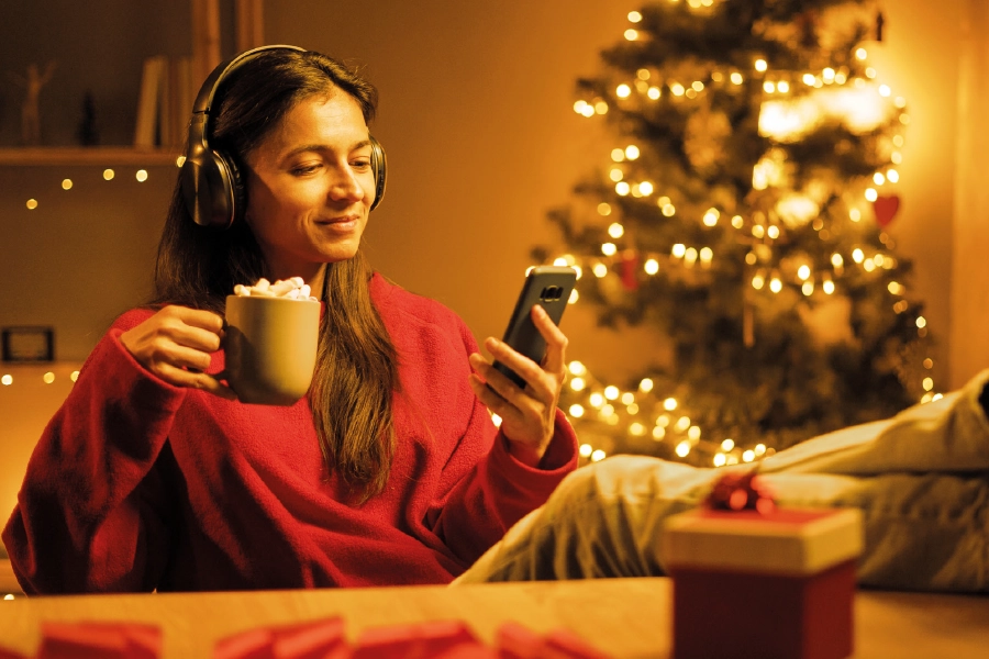A girl with a cup and a cell phone in a room with a Christmas atmosphere