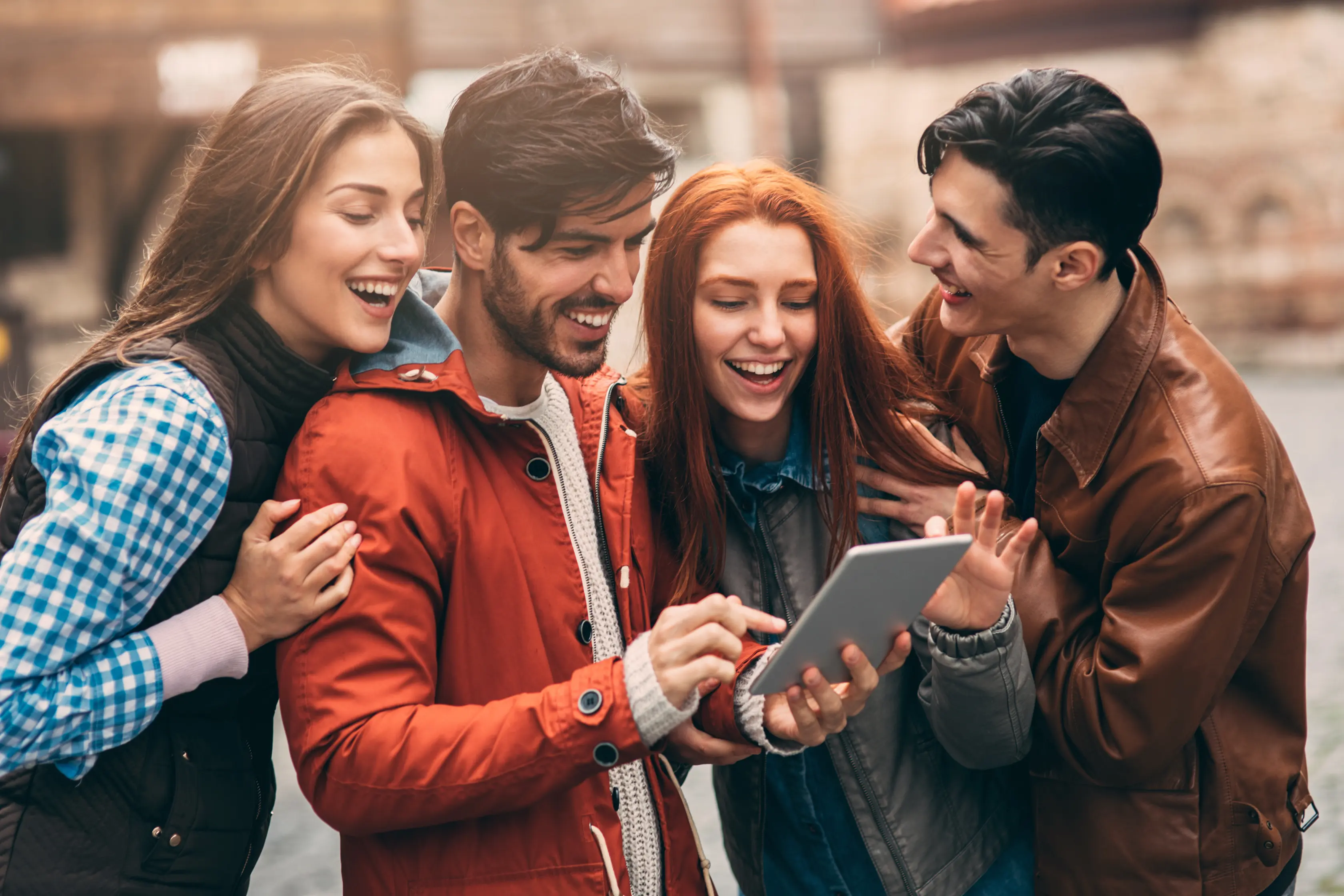 Quatro amigos sorridentes reunidos a olhar para um tablet que um deles segura.