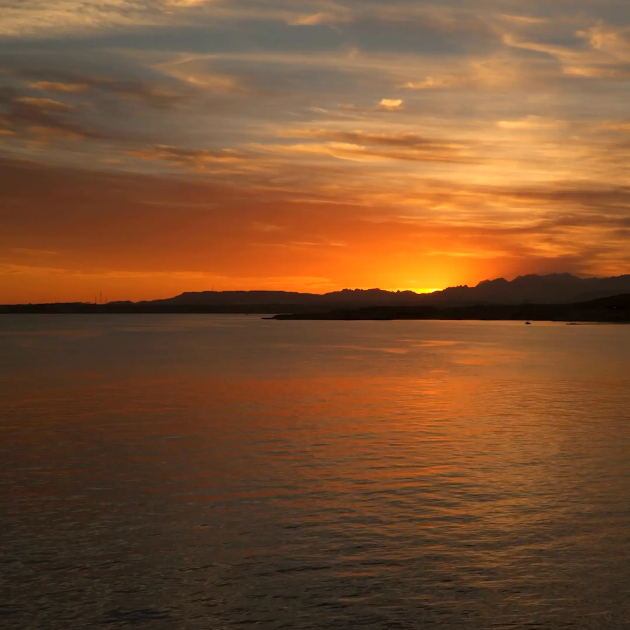 O sol a pôr-se sobre o mar, com a luz laranja a iluminar o céu e a água, e ilhas visíveis ao longe.