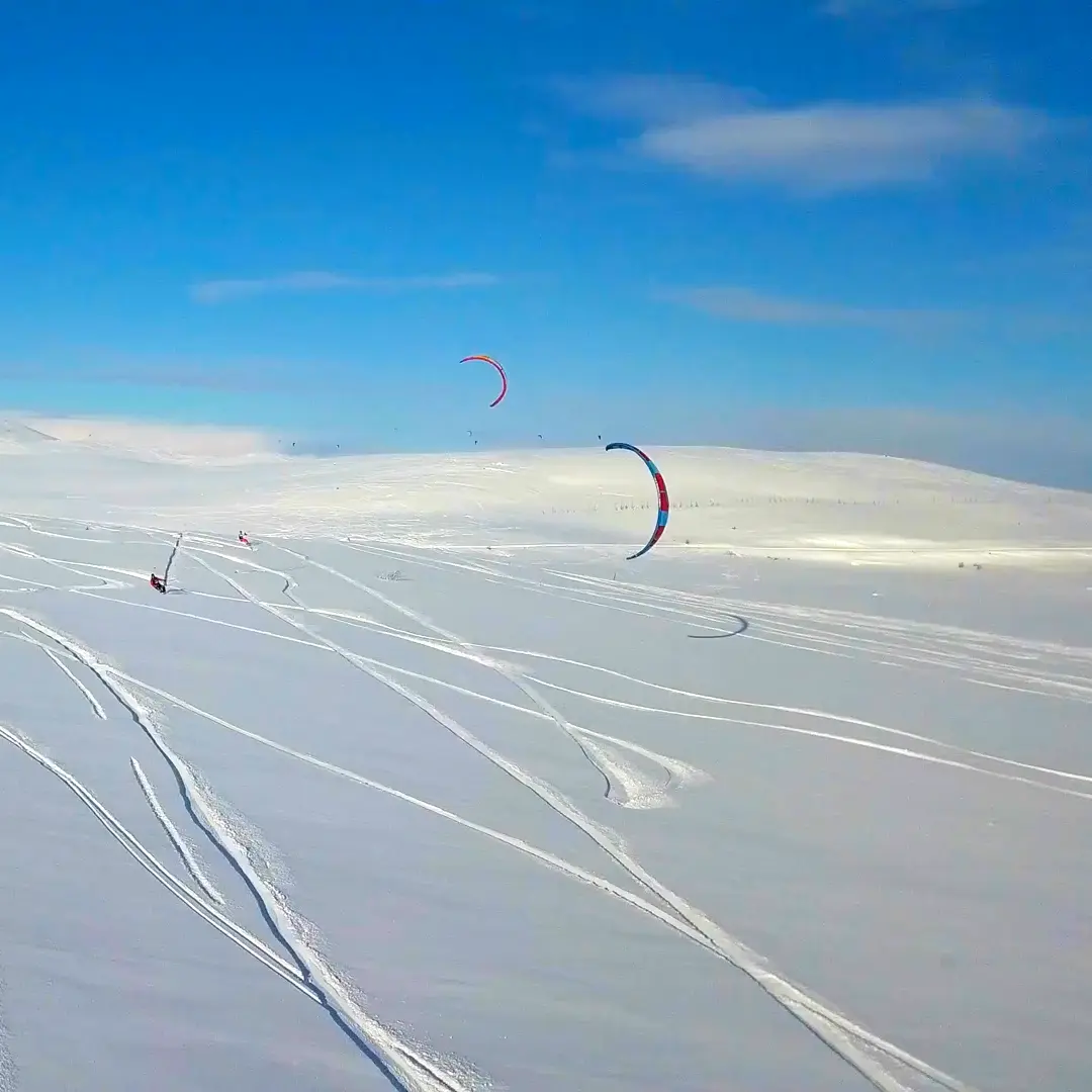 Paisagem de Inverno com neve e rastros, com praticantes de snowkite ao fundo.