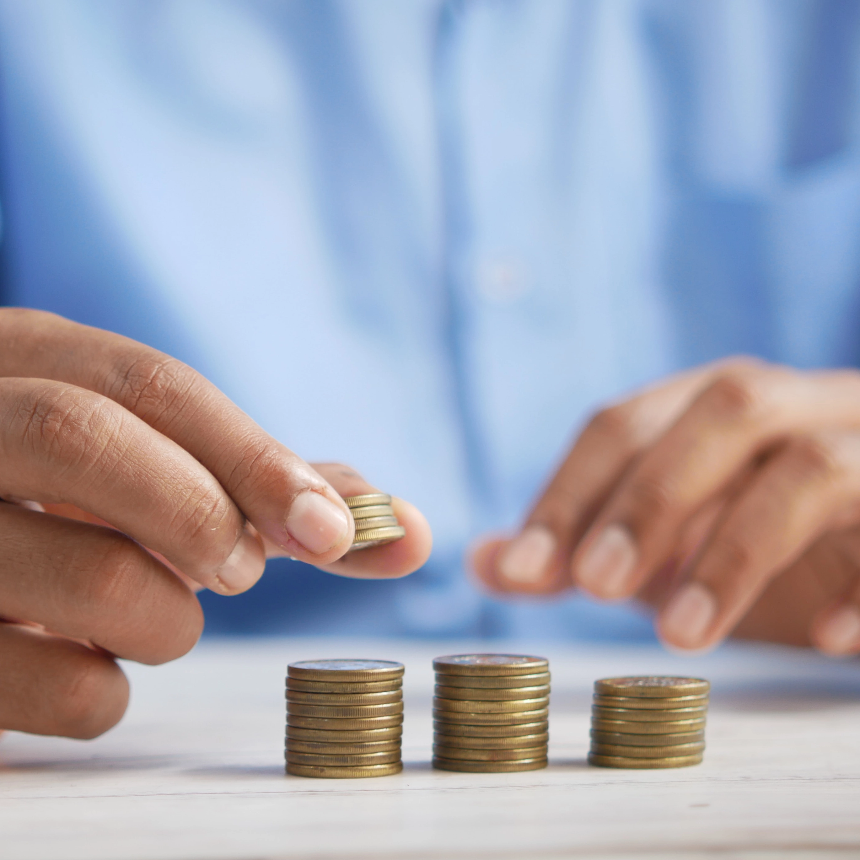 Mão a adicionar moedas a uma pilha crescente, simbolizando o crescimento financeiro.