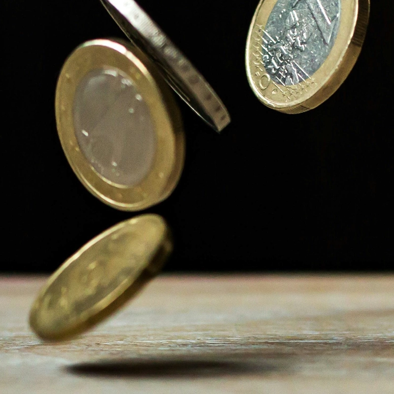 Moedas de euro a cair sobre uma superfície de madeira.