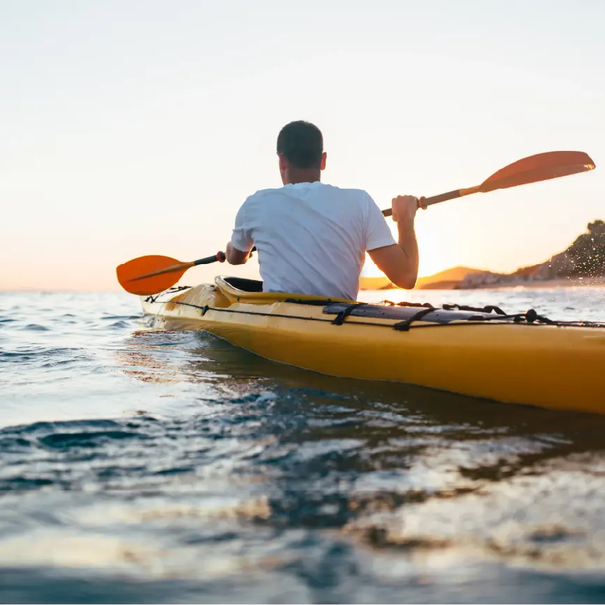 Pai e filho a praticar paddle numa lagoa calma, rodeados por natureza ao pôr do sol.