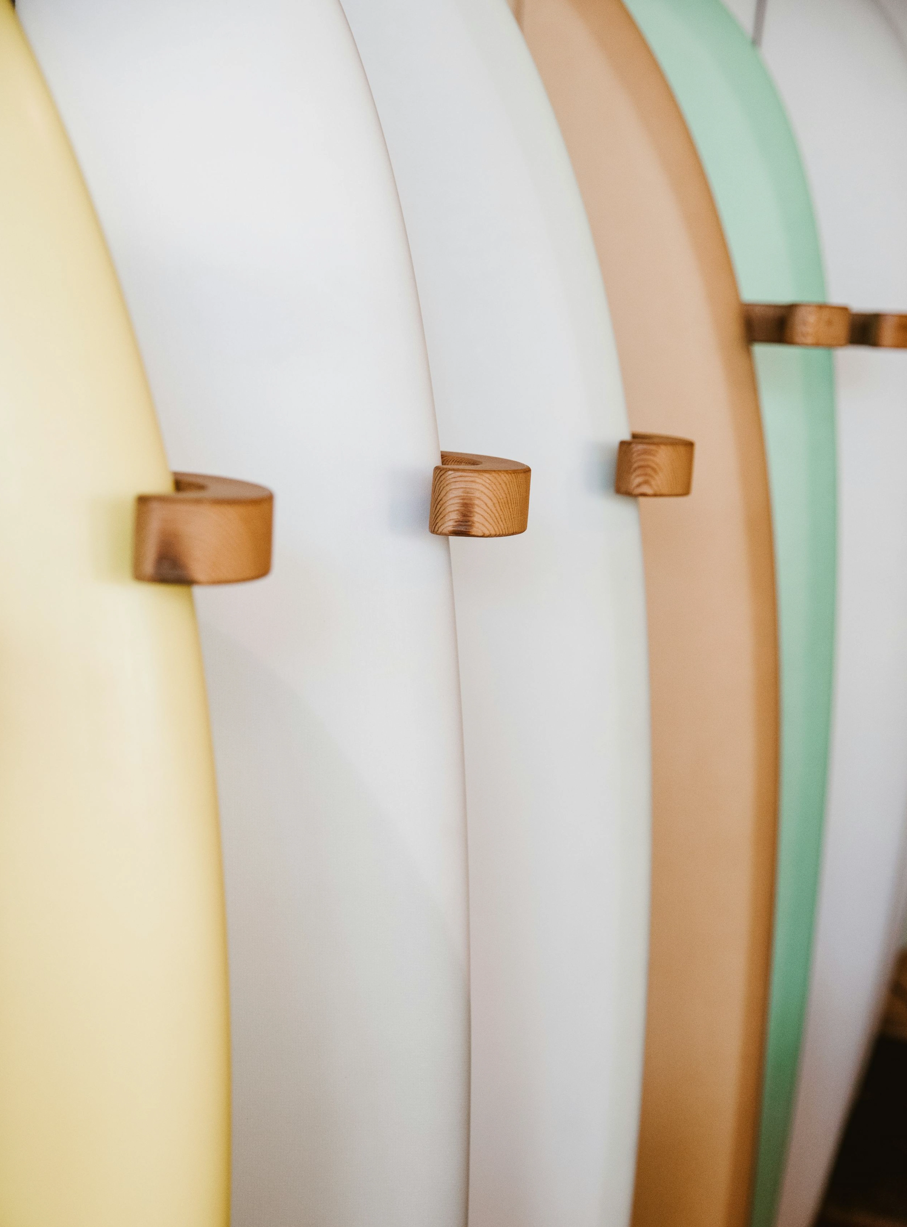Fileira de pranchas de surf em tons pastel, fixadas em suportes de madeira, simbolizando estilo de vida jovem e descontraído.