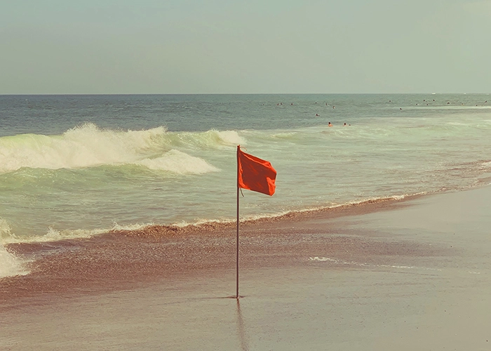 Bandeira vermelha numa praia, simbolizando atenção e cautela na seleção de Fundos de Investimento destacados pelo Banco Carregosa, alinhados com a conjuntura macroeconómica e os mercados financeiros.