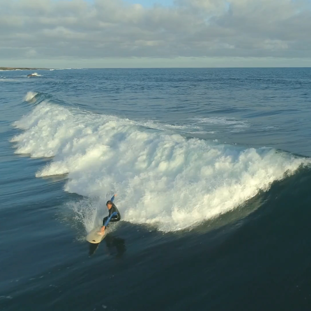 Prancha de surf na areia da praia, simbolizando um investimento descomplicado e acessível em ETFs, com a NextGen do Banco Carregosa.