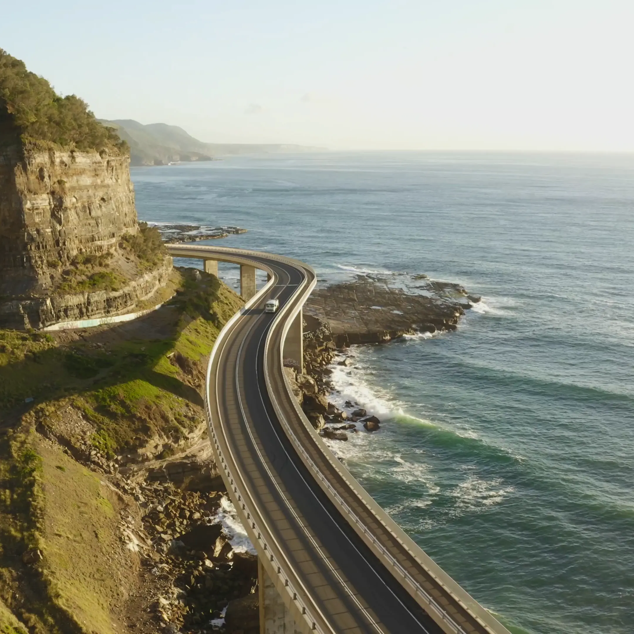 Vista aérea da Sea Cliff Bridge, uma estrada costeira com curvas sobre o oceano.