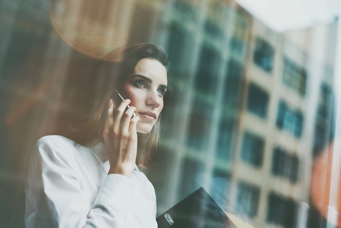 Mulher vestida formalmente, a fazer um telefonema num ambiente de escritório, simbolizando os serviços de intermediação financeira