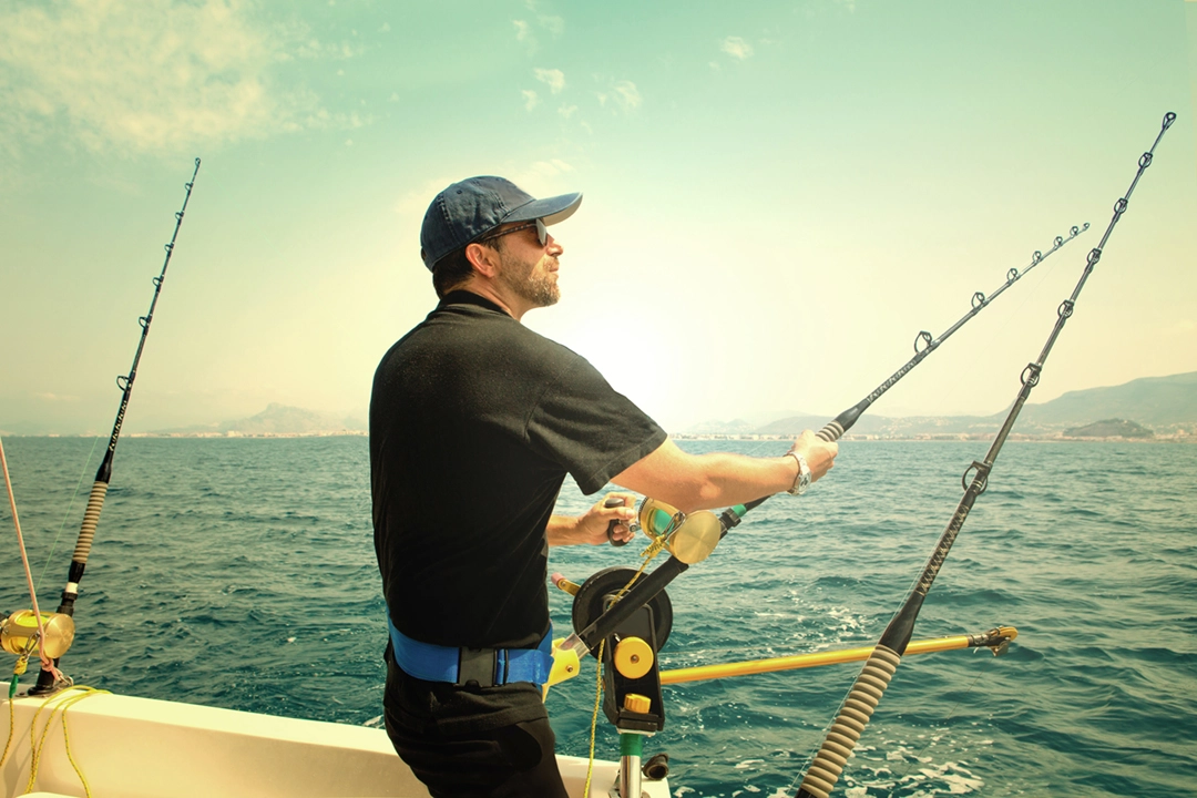 Pescador num barco com uma cana em momento de captura, com a movimentação calma do oceano