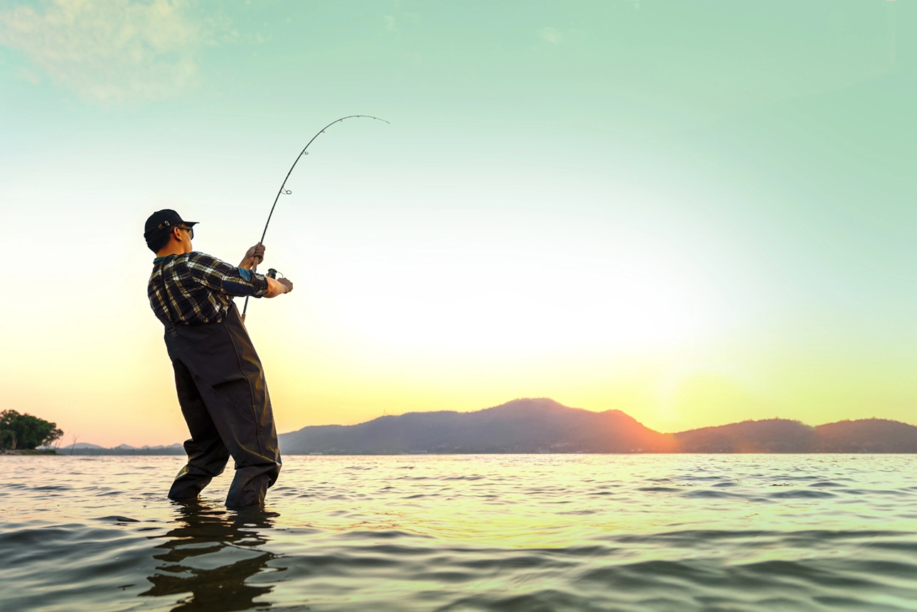 Pescador com jardineiras de pesca em momento de captura, com água que vai até aos pés