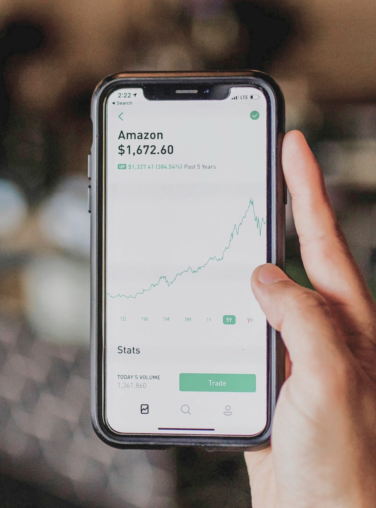 Mão a segurar um smartphone que apresenta uma aplicação de negociação de ações.
