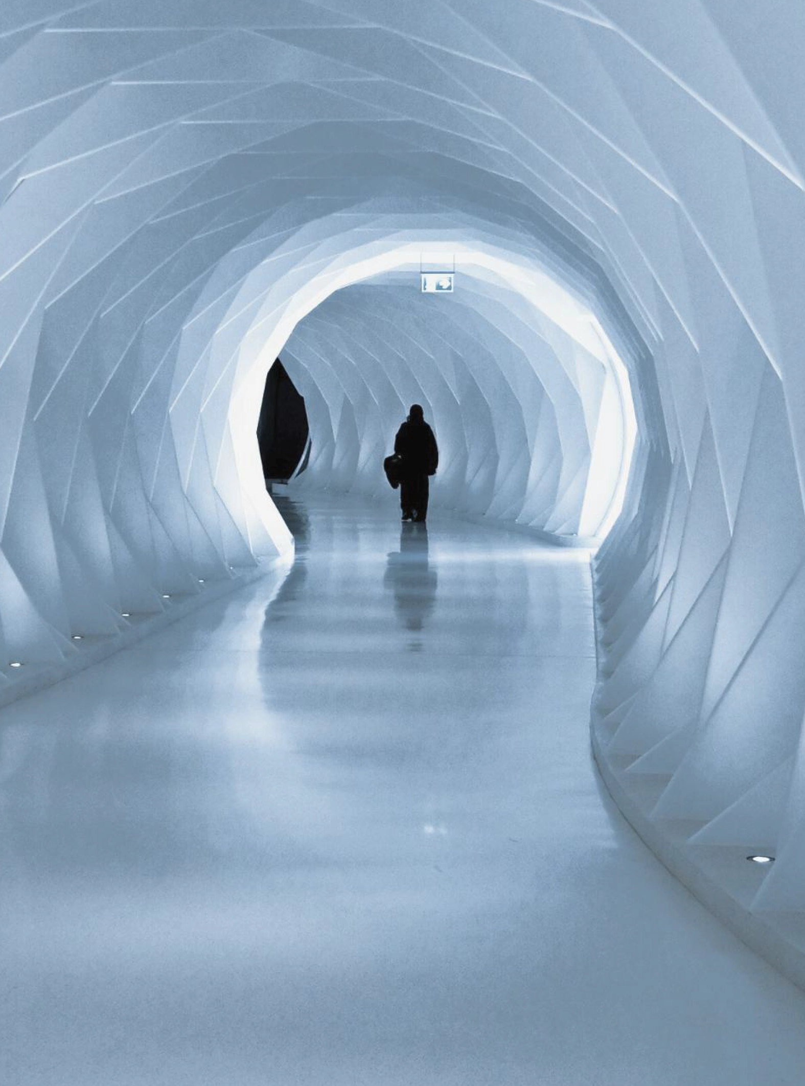 Uma pessoa a caminhar através de um túnel com uma estética semelhante a formações de gelo, iluminado por uma luz suave.