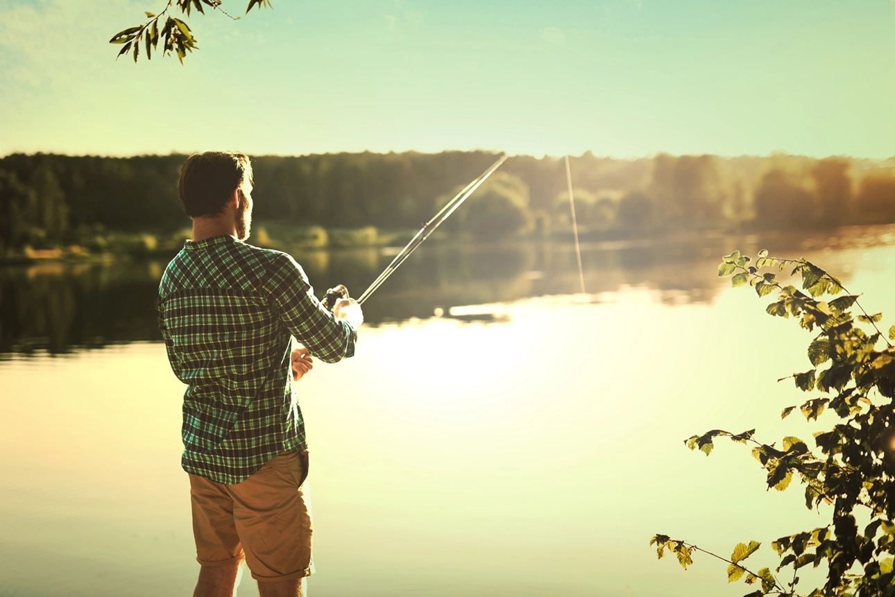 Plano das costas de um homem com uma cana de pesca, rodeado por uma ambiente tranquilo de natureza