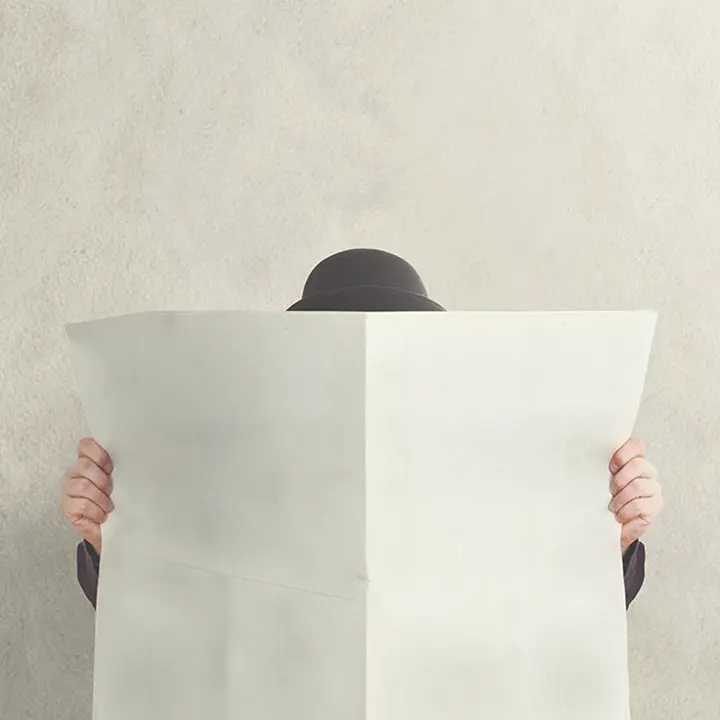 Person reading the newspaper with his face covered by it, symbolizing the importance of being informed and updated, particularly in terms of financial literacy